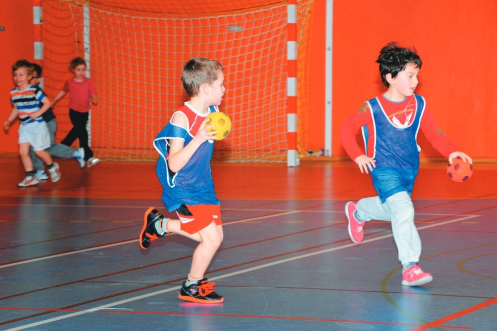 Deux petits garçons avec un chasuble bleu courant avec un ballon de handball dans les mains.